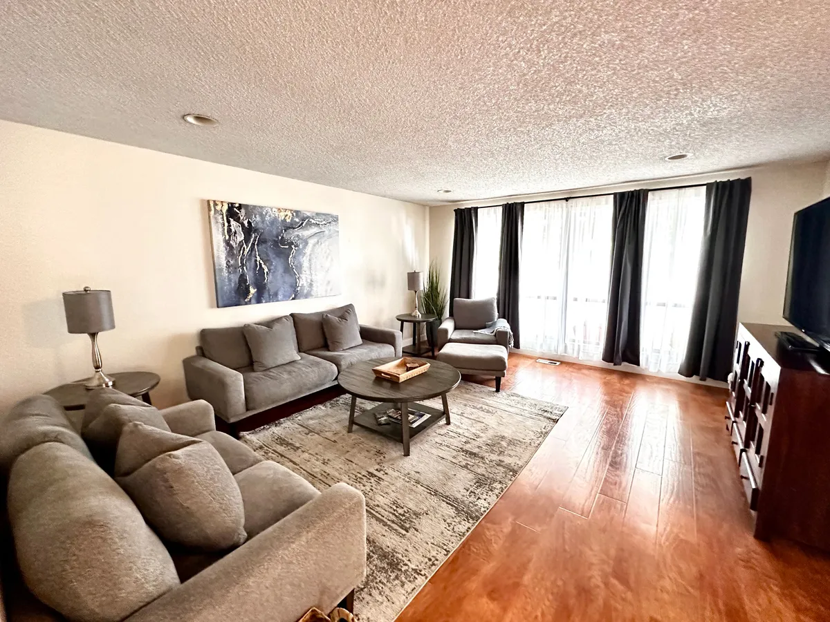 This inviting living room features a plush sofa set and accent chair arranged around a stylish coffee table, with warm lighting streaming through large windows dressed in soft curtains. Thoughtfully chosen artwork and modern decor create a cozy yet contemporary atmosphere, perfect for relaxing, socializing, or unwinding after a day exploring Medford.