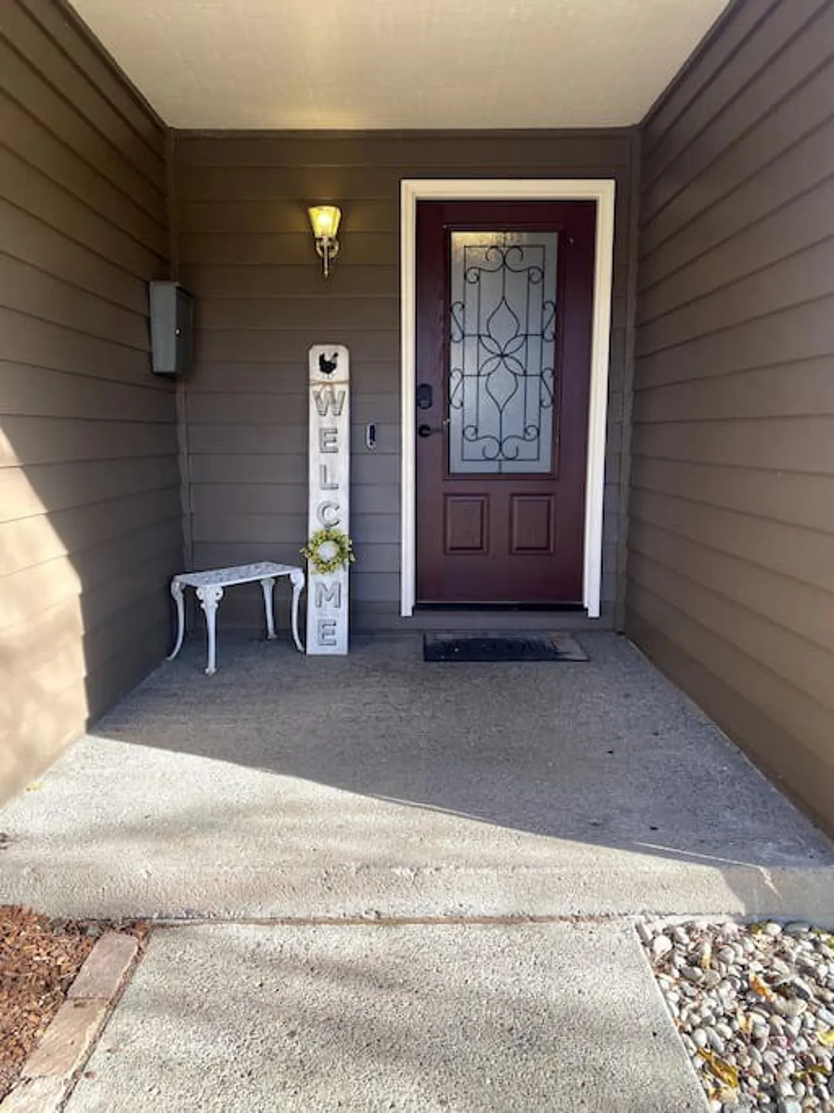 The image shows the exterior front door of the home, featuring a welcoming sign and a cozy bench. Seasonal decorations and tidy landscaping set a friendly and inviting tone, hinting at the peace and safety of the quiet cul-de-sac location.