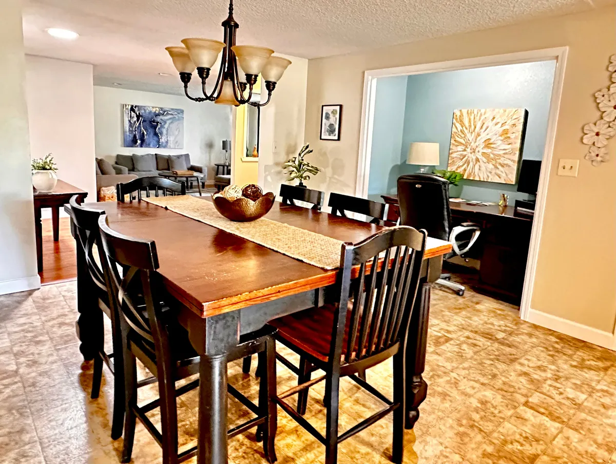 The dining area is elegantly staged with a large dining table under a chandelier, complemented by wall art and a cozy home office nook. The scene communicates a comfortable space for family dinners, social events, and productive work sessions, emphasizing versatility and a welcoming mood.