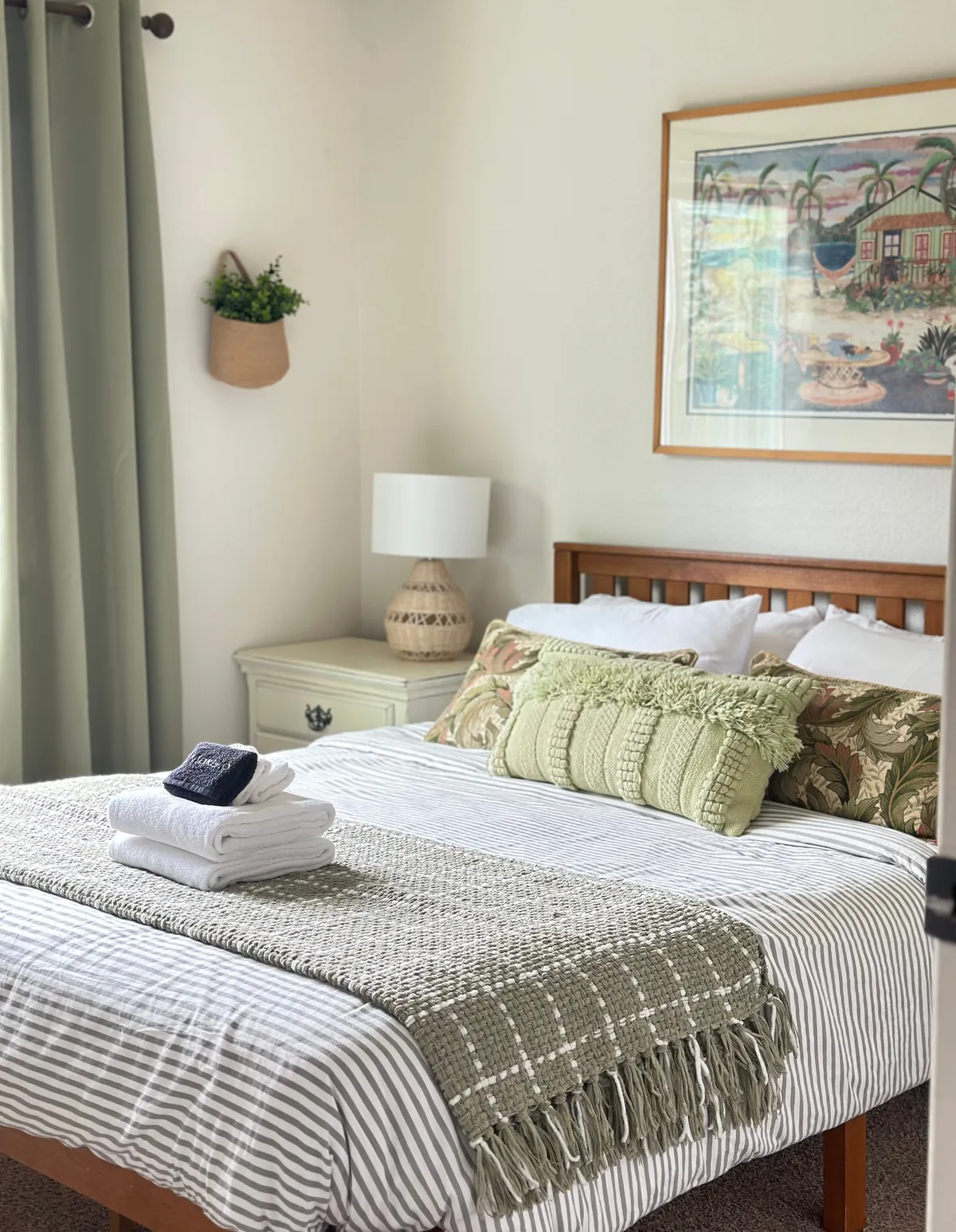 A cozy master bedroom with a prominent bed adorned with decorative pillows, complemented by green curtains, wall art, and a nightstand with a lamp. The tranquil, inviting atmosphere suggests a restful retreat ideal for relaxation at day's end.