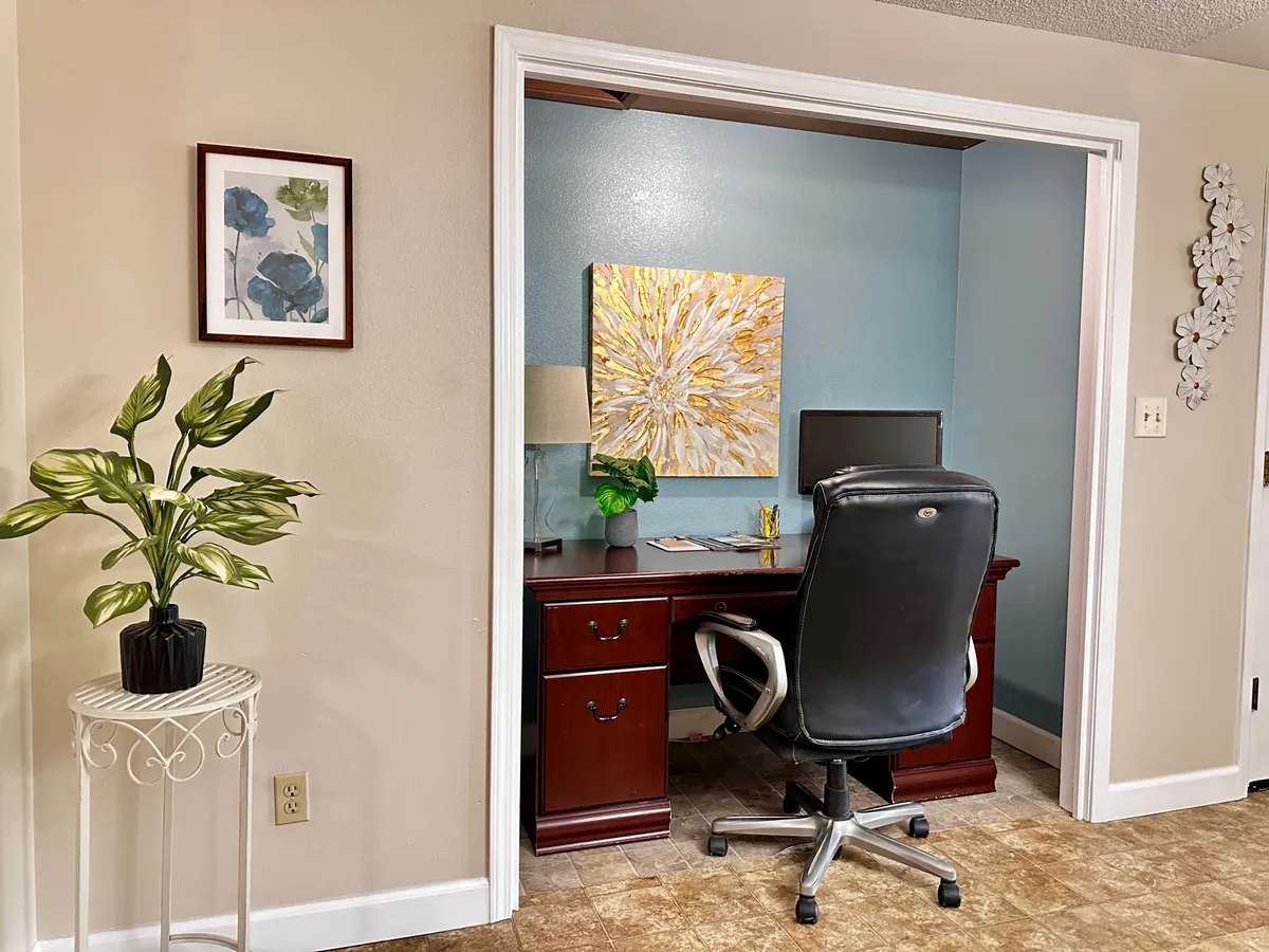 A thoughtfully arranged workspace featuring a desk with a comfortable chair, modern artwork, and a lush houseplant. The setup is designed for maximum productivity and creativity, with ample natural light and a calm atmosphere.