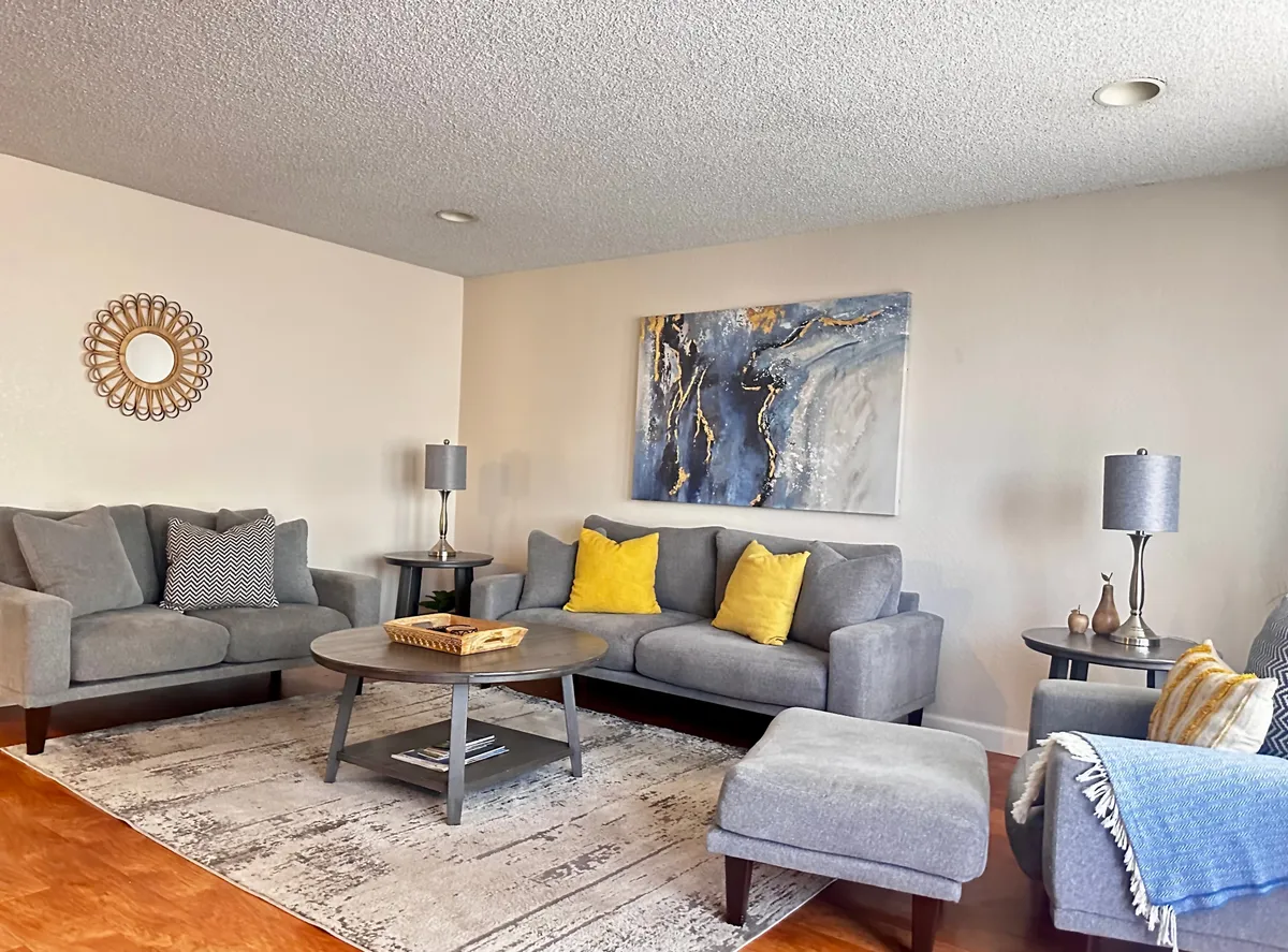 This image features a cozy living room setup with sofas, a coffee table, artwork, and a mirror. The arrangement is inviting for both casual lounging and socializing, with ample space for relaxing and gathering. The presence of comfortable seating and a central table makes it ideal for shared activities like watching movies or having conversations.