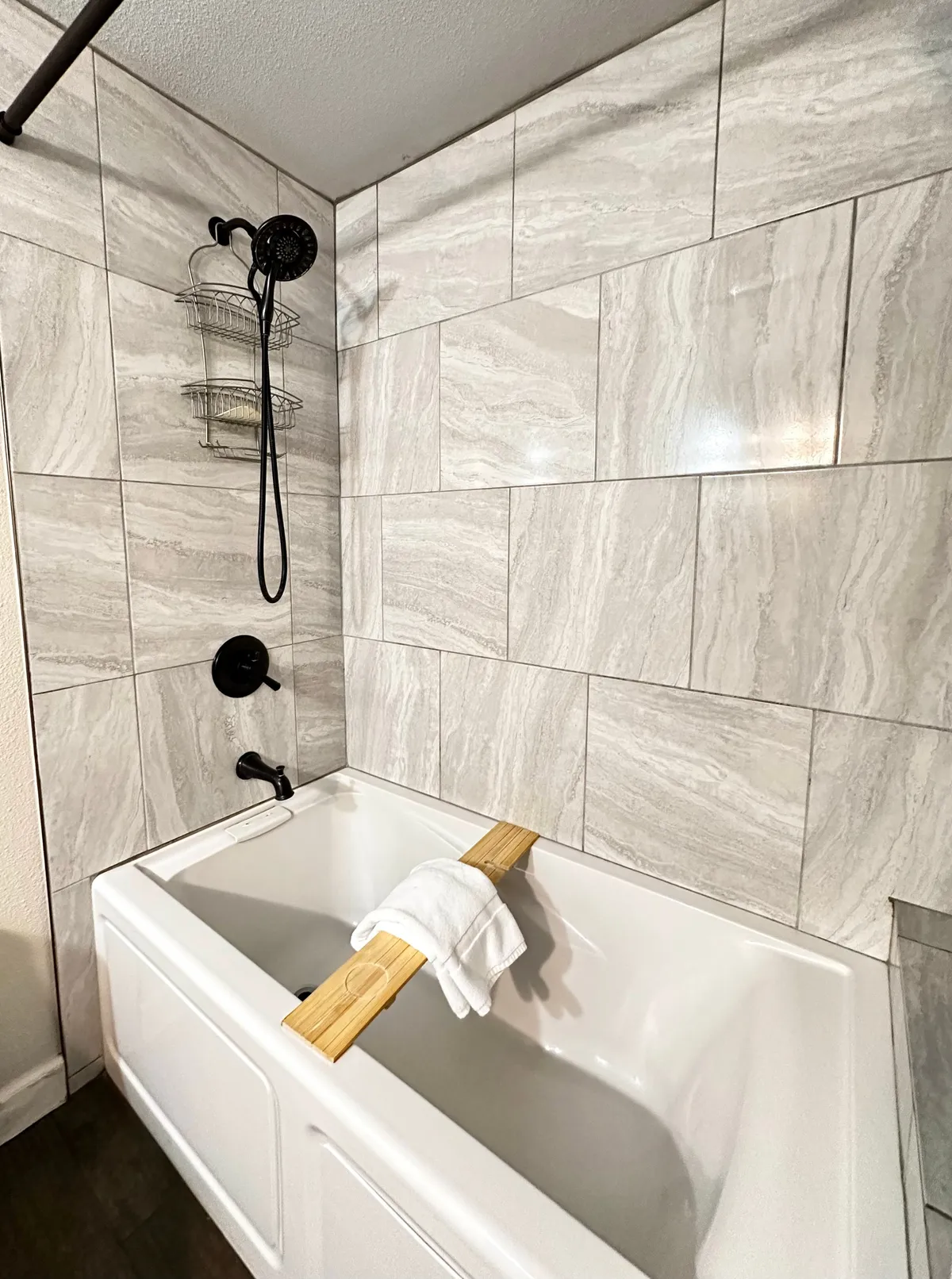 A tranquil bathroom scene with a deep soaking tub, elegant showerhead, fluffy towel, and a wooden bath tray perfect for reading or pampering rituals. The setting exudes spa-like tranquility and indulgence.