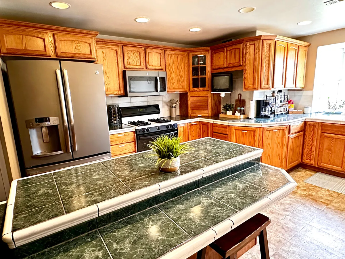 A bright and functional kitchen scene showcasing a large island, stainless steel appliances, upper and lower cabinetry, and a window that brings in abundant natural light. The layout highlights ample counter space for meal prep and socializing, with a welcoming atmosphere for hosting and family gatherings.